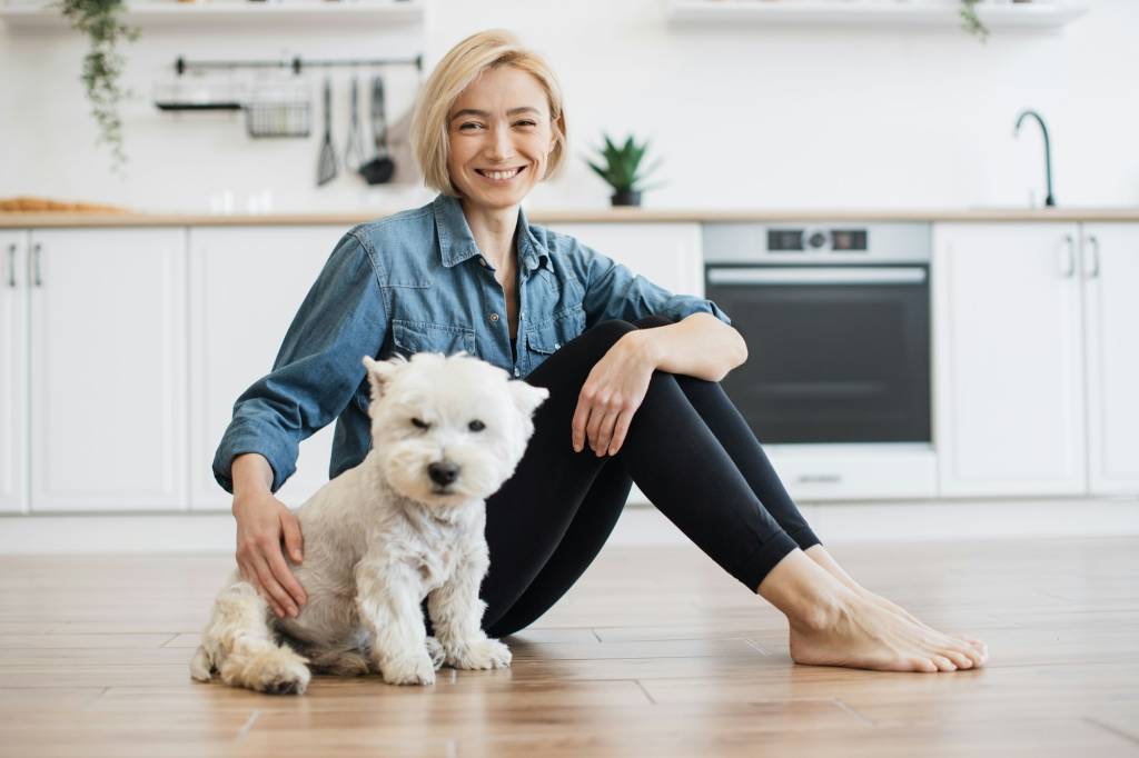 Lady sitting next to white dog on floor in apartment